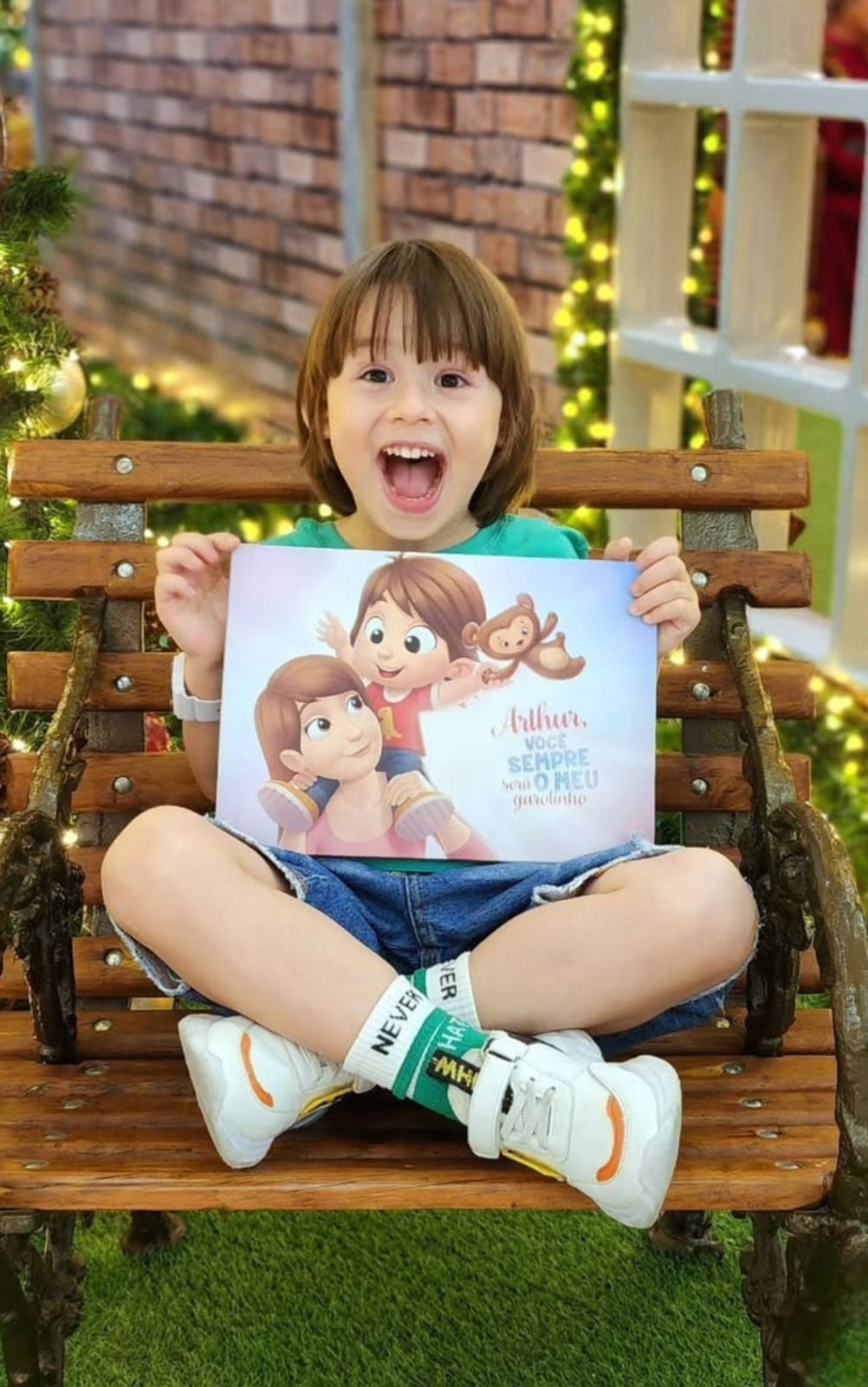 Menino sentado num banco, sorrindo e mostrando com orgulho o seu livro personalizado